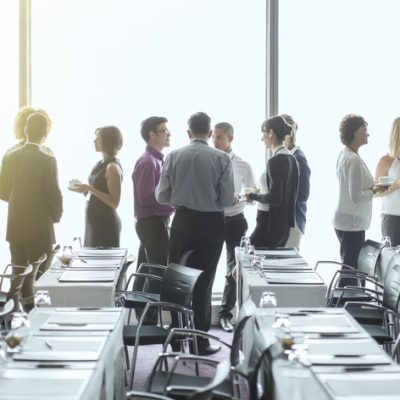 Group of people standing by windows of conference room, socializing during coffee break